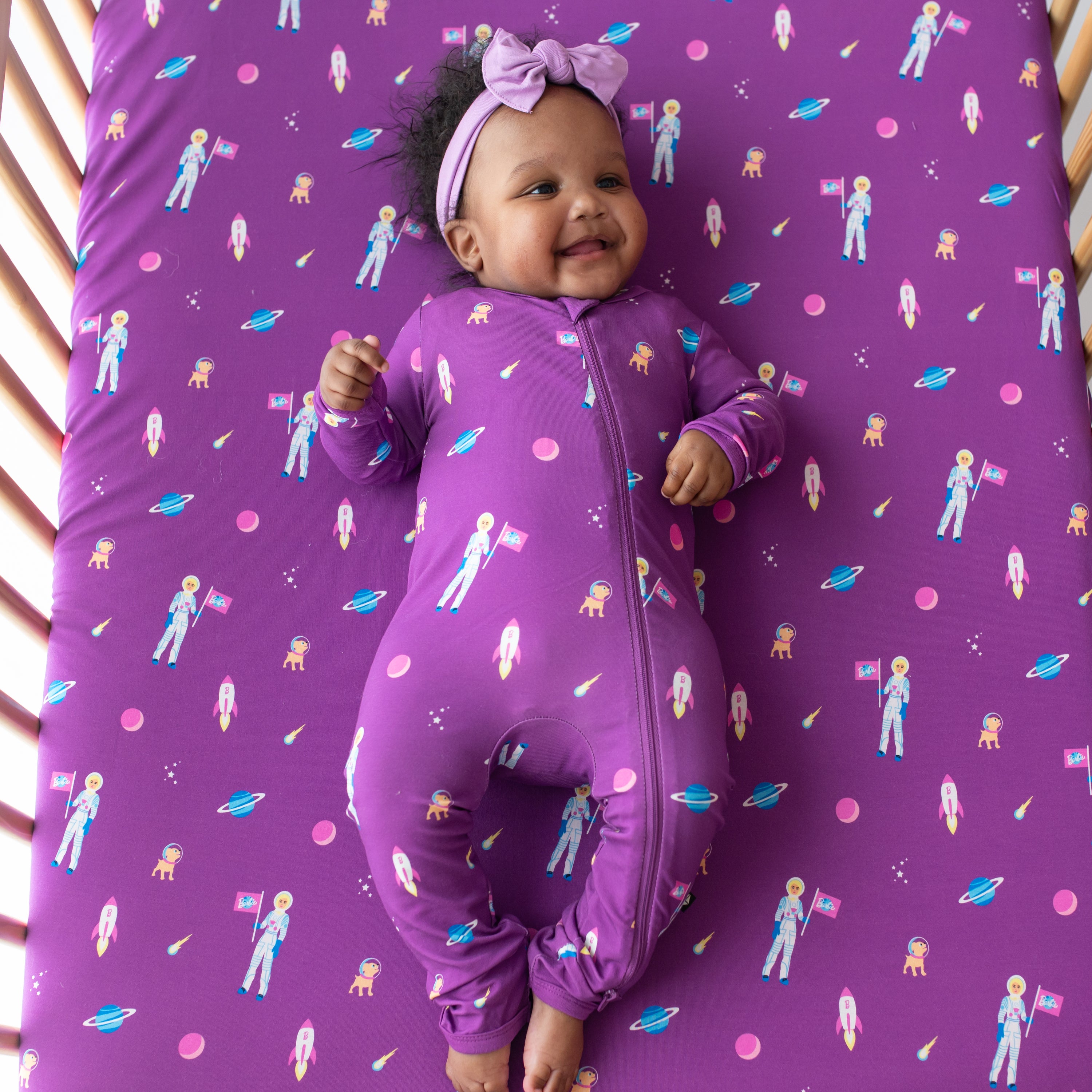Infant laying on Kyte Baby Crib Sheet and wearing Zippered Romper pajamas in Barbie™ Astronaut