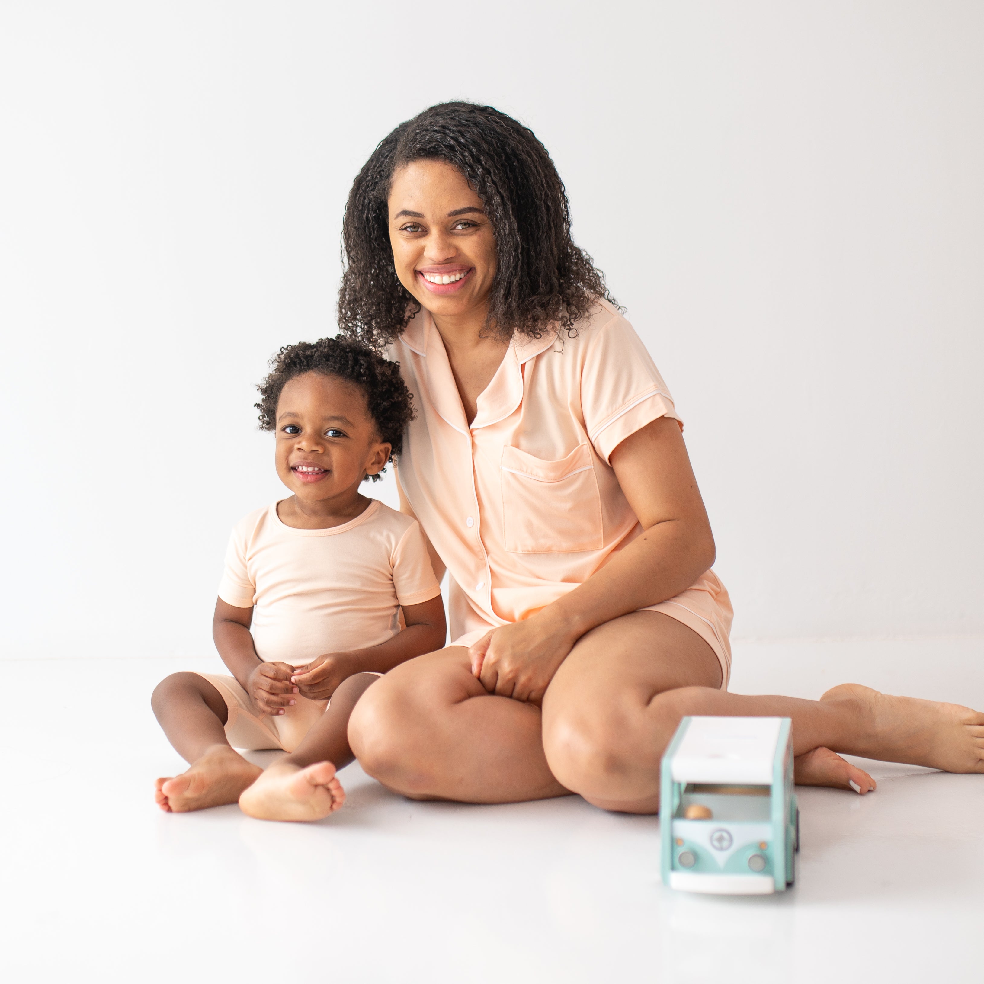 Smiling model sitting wearing the Women's Short Sleeve Pajama Set in Canyon with her child wearing the Toddler Short Sleeve Pajama Set in Canyon