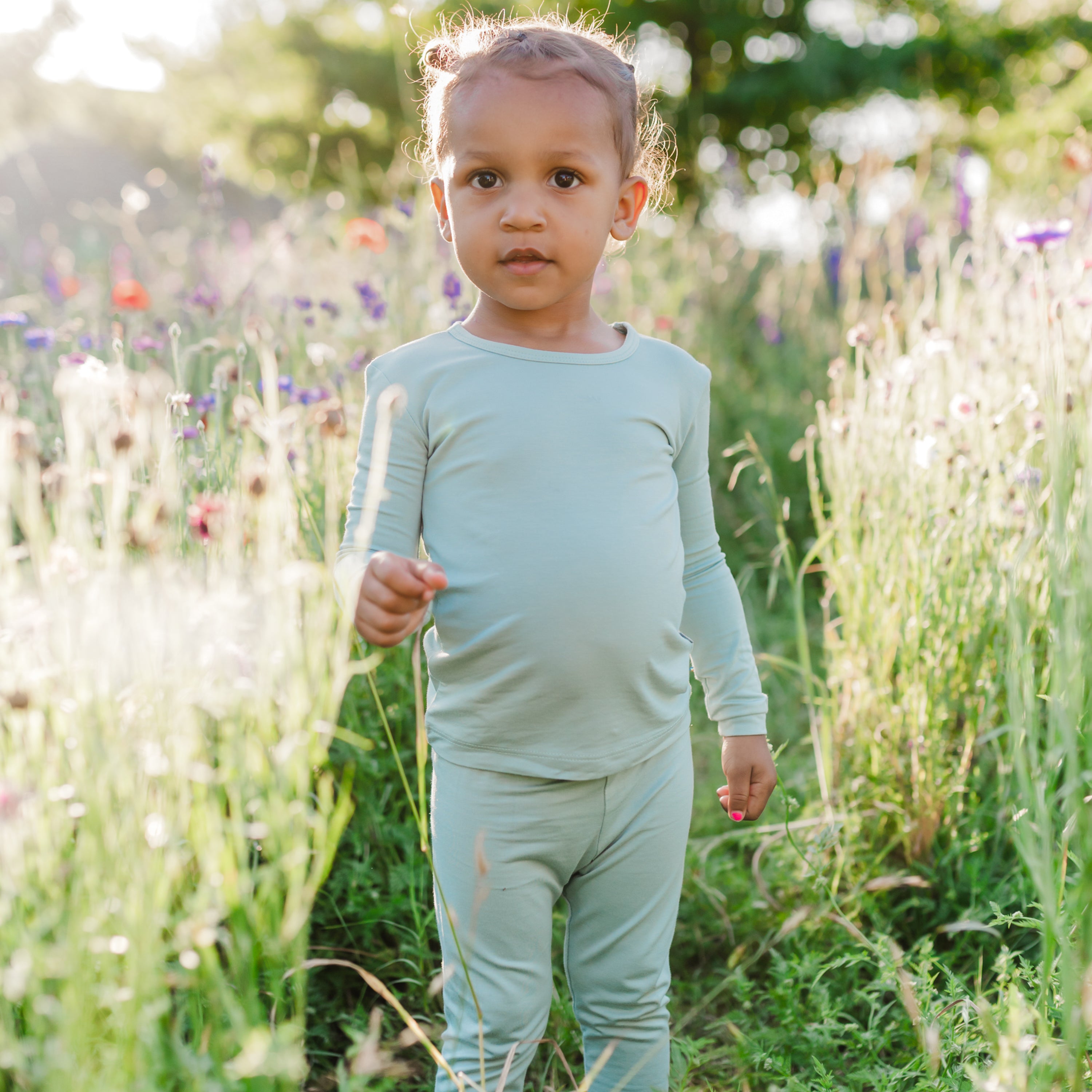 Toddler modeling Long Sleeve Pajamas in Sage in a wildflower field