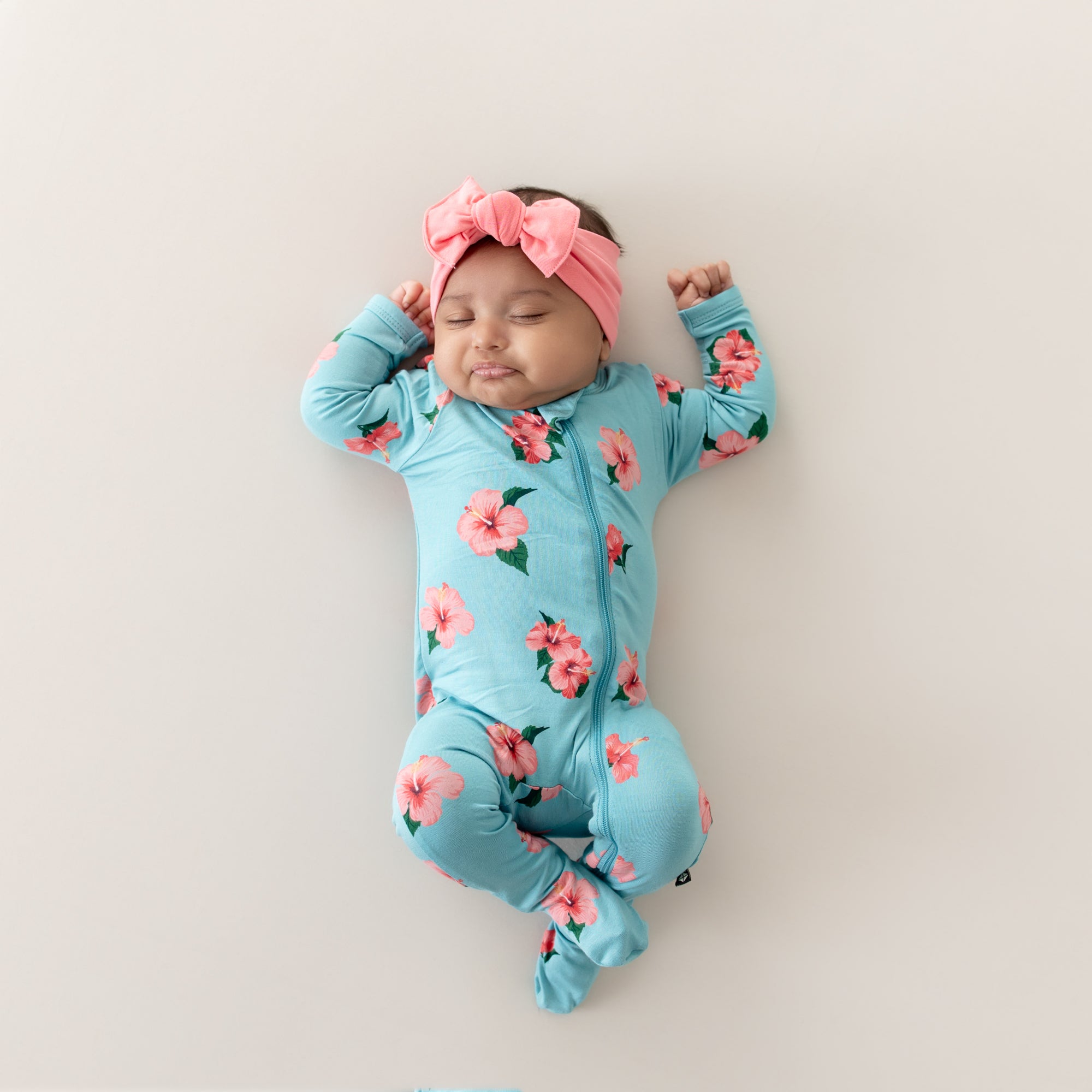 Baby wearing Zippered Footie in Hibiscus with matching pink bow headband