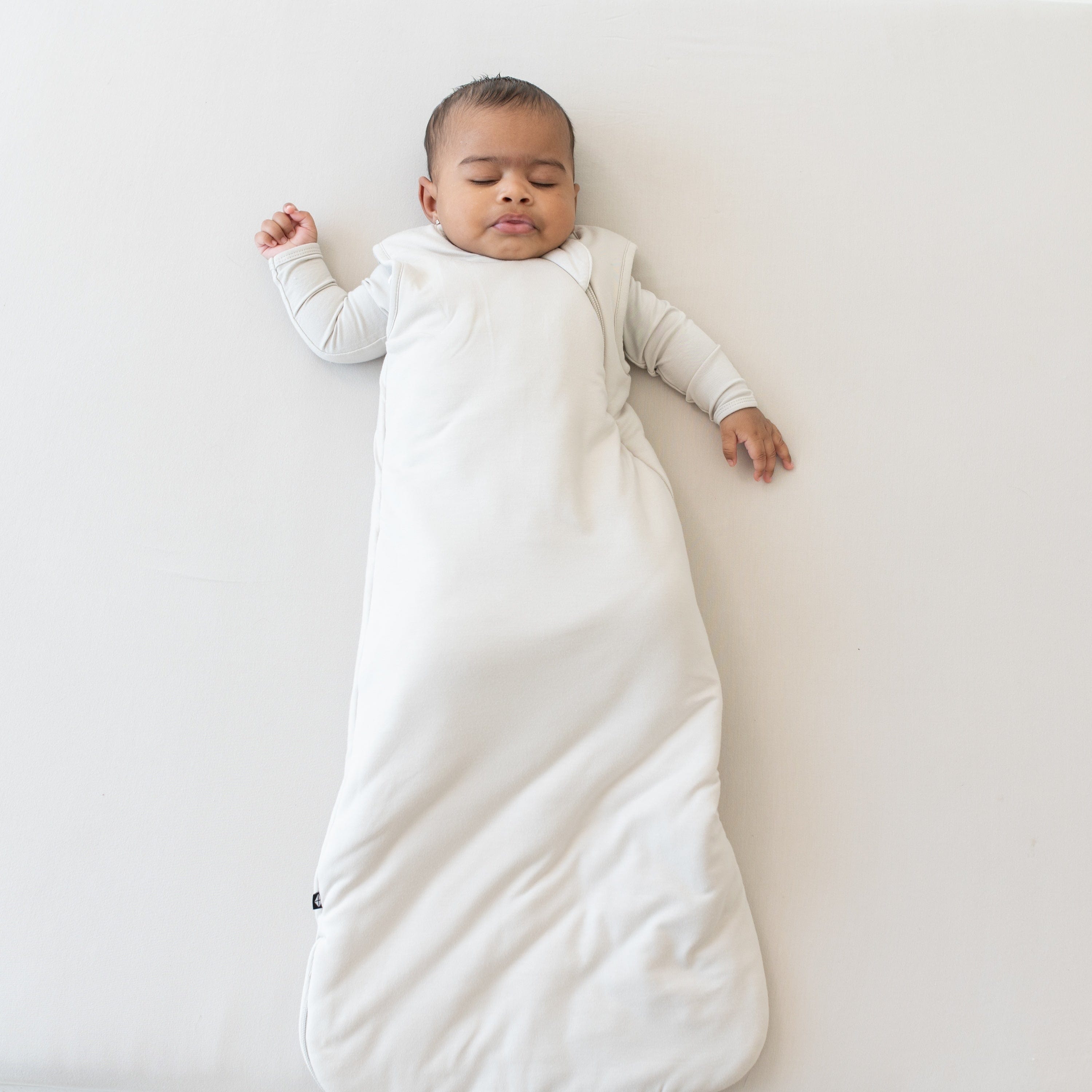 Sleeping baby wearing the Sleep Bag in Oat  2.5 with an Oat long sleeve romper underneath