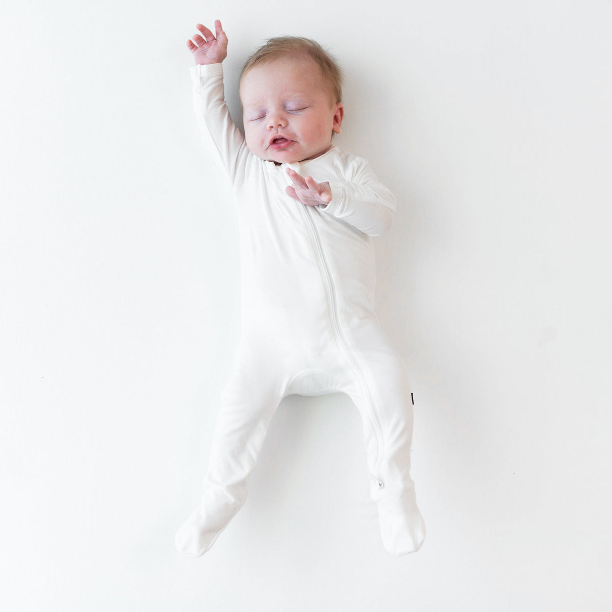 Infant sleeping with hand up over the head wearing the Zippered Footie in Cloud