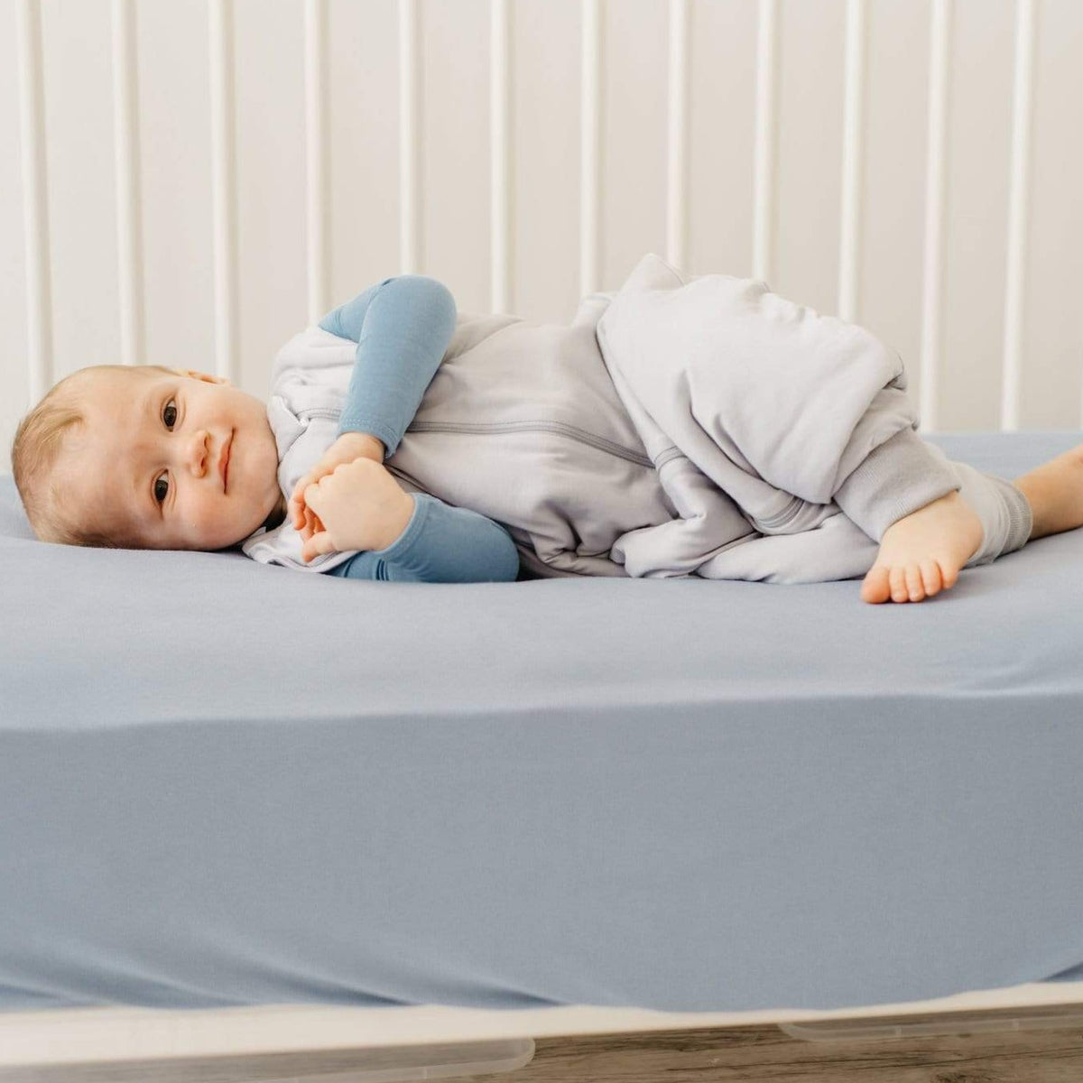 Toddler laying in a crib on their side while wearing Kyte Baby Sleep Bag Walker in Storm 1.0